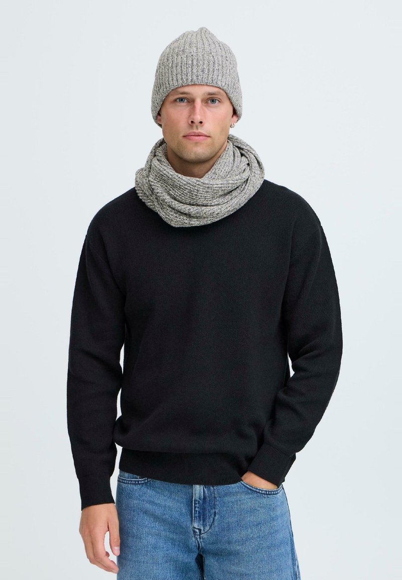 Maglione nero a maglia, berretto a coste grigio chiaro e sciarpa ad anello. Il maglione ha un colletto a girocollo e una vestibilità casual; la sciarpa presenta un motivo testurizzato.