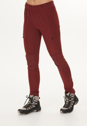 Pantalons de yoga rouges extensibles avec une taille élastique et des poches latérales zippées, associés à des bottes de randonnée noires avec des accents gris et des fermetures à lacets.