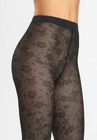 Czarne legginsy w kwiatowy wzór, wykonane z przejrzystego materiału, z wysokim pasem i skomplikowanymi wzorami kwiatów na całej tkaninie.