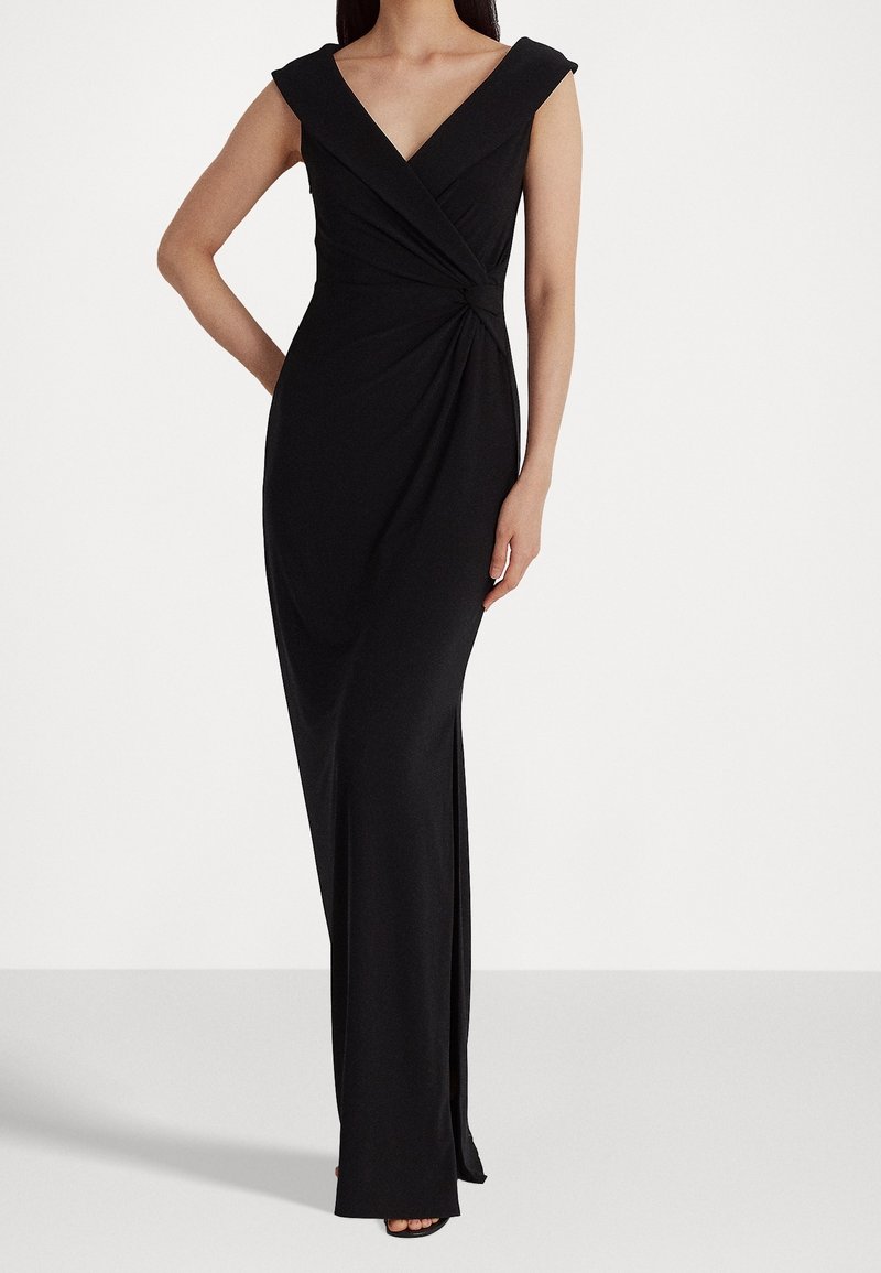 Langes schwarzes Kleid aus dehnbarem Stoff mit V-Ausschnitt, kurzen Puffärmeln und verdrehtem Frontdetail. Verfügt über einen seitlichen Schlitz für mehr Bewegungsfreiheit.