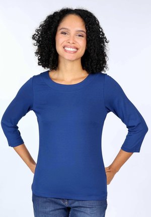 Blaues Langarmshirt aus weichem, dehnbarem Stoff mit Rundhalsausschnitt und Dreiviertelärmeln, kombiniert mit Jeans.
