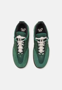 Green Nike sneakers feature a mix of mesh and suede materials, a rounded shape, white laces, and subtle perforations on the sides.