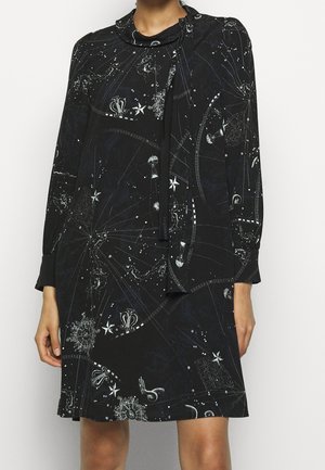 Zwarte jurk met een kosmisch patroon van sterren en hemelse motieven. Zacht materiaal, lange mouwen en een strikdetail bij de hals.