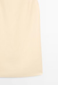 Primo piano della sezione inferiore di una gonna beige semplice con orlo dritto su sfondo bianco.