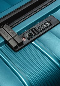 Valise turquoise avec une surface texturée, verrou TSA noir et serrure à combinaison à cadran avec un fermoir en métal argenté pour plus de sécurité.