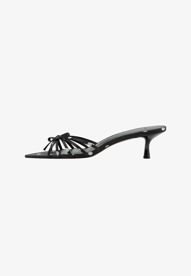 Mule noire à bout ouvert avec fines brides, détail nœud, petit talon kitten et motif à pois blancs sur les brides et la semelle.