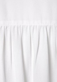 Weißer Stoff mit einer weichen, glatten Textur, der entlang der Naht mit gerafften Details versehen ist, um zusätzliche Dimension und subtile Designinteressen zu bieten.