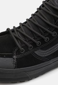 Baskets montantes noires avec des lacets ronds épais, tige en daim et mesh, coutures renforcées et semelle en caoutchouc texturée.