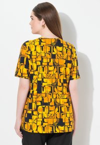 T-shirt a maniche corte con un motivo geometrico giallo e nero, realizzato in morbido tessuto con una vestibilità comoda e scollatura rotonda.