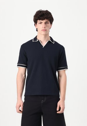 Polo shirt navy avec un col en V, un col blanc contrastant et des poignets de manches rayés. Fabriqué dans un tissu doux, avec une coupe décontractée.