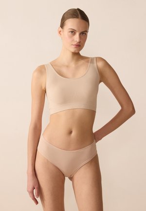 Top corto beige senza cuciture con spalline larghe e finitura liscia, abbinato a culotte in vita alta dello stesso colore, entrambe in tessuto elasticizzato.