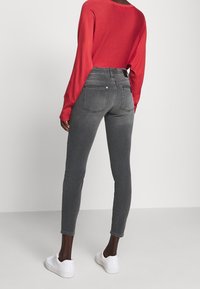Jeans de mezclilla gris con una cintura alta y un diseño ajustado. Cuenta con bolsillos traseros y costuras sutiles. Combinados con una blusa roja de manga larga y zapatillas blancas.