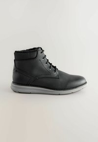 Bota de tobillo de cuero negro con un cuello texturizado, punta redonda, cordones de seis ojales y una suela de goma gris con detalle de costura.