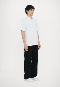 Hvit kortermet polo skjorte med klassisk krage, sammen med svarte vide bukser og hvite sneakers. Minimalistisk design uten mønstre.