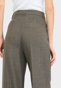 Pantaloni a vita alta con motivo a occhio di pettine, realizzati in un tessuto strutturato e lavorato; presentano tasche laterali e una tasca posteriore discreta.