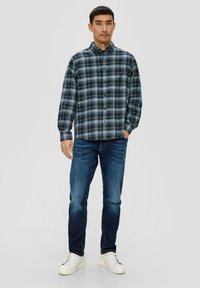 Chemise à carreaux dans des nuances de bleu et de noir, associée à un jean bleu et des baskets blanches, avec des manches longues et une coupe décontractée.