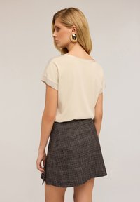 Top beige a maniche corte con una texture liscia abbinato a una mini gonna a quadri scura con una leggera linea ad A e uno spacco laterale.