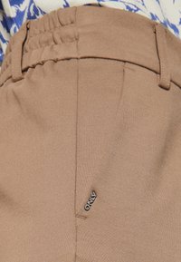 Beige bikses ar elastīgu jostasvietu un sānu kabatām. Uz priekšu, netālu no jostas, redzams ievērojams zīmola logo "ONLY".
