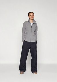 Halli fliisist lukuga jope kõrge kraega, mis on kombineeritud lahtiste mustade taskutega ning lõdva lõikega cargo-pükstega.