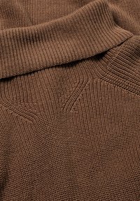 Tissu marron tricoté avec une texture côtelée, présentant un col épais et plié ainsi qu'un détail de motif subtil le long des coutures.