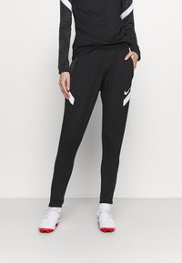 Svarta atletiska byxor med vita sidodetaljer och midjeband med dragsko, tillverkade av ett lätt material, med en slim fit-design.