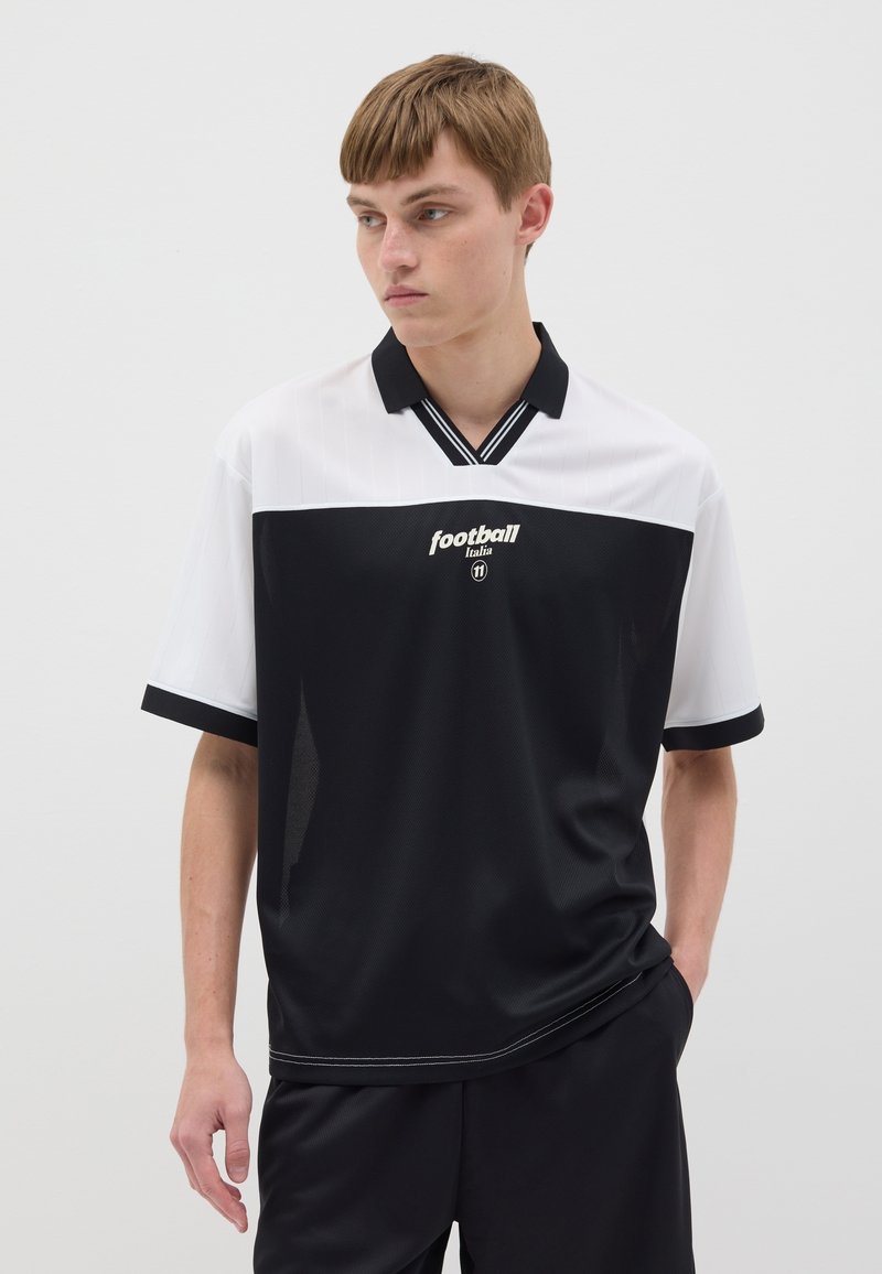Chemise à manches courtes noir et blanc avec un col en V, présentant des rayures verticales, le logo "football Italia" et un tissu lisse et respirant.