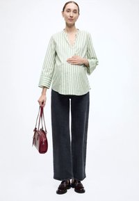 Πουκάμισο με πράσινες και λευκές ρίγες, V-λαιμόκοψη και φαρδιά μανίκια, σε συνδυασμό με σκούρο παντελόνι φαρδιάς γραμμής. Αξεσουάρ περιλαμβάνουν μια μπορντό τσάντα και σκούρα παπούτσια.