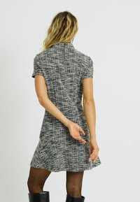 Vestido de manga corta en tejido texturizado blanco y negro, con cuerpo ajustado y falda acampanada, con detalle de cremallera en la parte trasera.