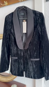 Blazer preto em veludo com colarinho de seda em contraste. Tecido texturizado com riscas verticais. Duas bolsos frontais e uma etiqueta visível.