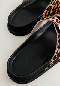 Tongs à motifs léopard avec une semelle en caoutchouc noir, dotées d'un matériau texturé et d'une semelle intérieure lisse pour le confort. Logo de la marque visible.