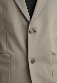 Beige blazer med slagkrage, to frontlommer og to knapper med en subtil glans. Glat tekstur, skræddersyet pasform.