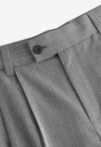 Pantalons plissés gris en tissu texturé avec un motif chevron, complétés par une fermeture à bouton noir et une taille droite.