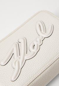 Clutch in pelle crema con lettering in rilievo "Noël" in una finitura bianca liscia. Superficie testurizzata con dettagli di cucitura visibili.