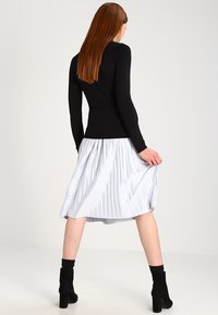 Schwarzes, enganliegendes Langarmoberteil kombiniert mit einem knielangen silbernen Plisseerock. Das Outfit wird durch schwarze Absatzstiefel ergänzt.