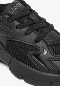 Black athletic shoe featuring a mix of textured mesh and smooth synthetic materials, with black laces and a subtle logo on the tongue.