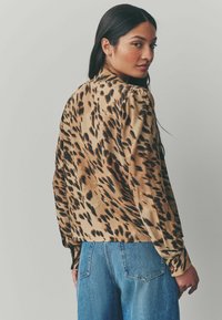 Blouse à imprimé léopard en beige et noir, avec des manches longues, des épaules froncées et une coupe décontractée, associée à un jean taille haute.
