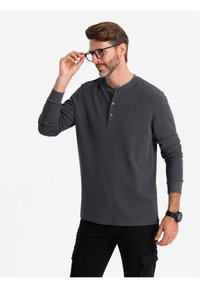 Maglietta henley grigia a maniche lunghe con tre bottoni al collo; presenta una texture morbida e maniche aderenti, abbinata a pantaloni cargo neri.