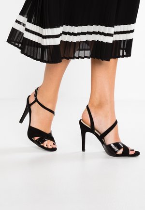 Schwarze High Heels Sandalen mit überkreuzten Riemen aus Wildleder und lackierter Optik, mit offenem Zehenbereich und schlankem Stiletto-Absatz.