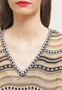 V-ringad tröja med flerfärgade horisontella ränder, med en strukturerad stickning, svart och vit geometrisk kant, samt ljusa metalliska accenter.