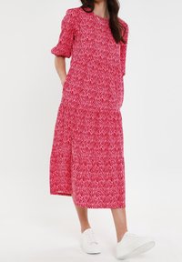 Vestido rojo de longitud media con un patrón ondulado blanco, mangas cortas abullonadas y bolsillos laterales, combinado con zapatillas blancas.