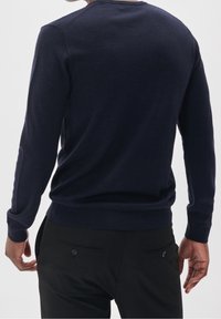 Granatowy dziany sweter z długimi rękawami, okrągłym dekoltem i dopasowaną talią. W zestawie z czarnymi spodniami z tylnymi kieszeniami.