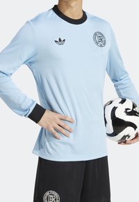 Ljusblå långärmad fotbolls tröja med ribbad textur och svarta detaljer vid kragen och ärmsluten, med en logotyp på bröstet.