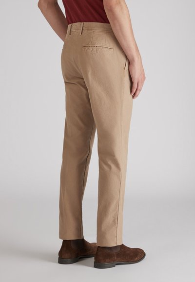 Beżowe bawełniane spodnie z prostymi nogawkami, z tylnymi kieszeniami i widocznymi detalami szycia, w zestawieniu z brązowymi zamszowymi botkami za kostkę.