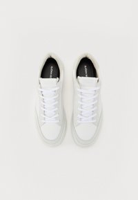 Hvide sneakers med en glat læderoverdel, polstret krave og flade hvide snørebånd. Sorte indersåler med branding synlig på tungen.