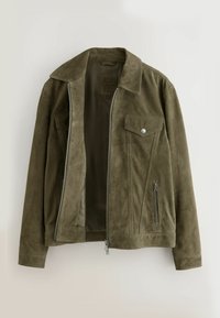 Alyvuogių žalios spalvos zomšinė striukė su sidabriniu užtrauktuku, krūtinės kišenė su sagtele ir šonine kišene su užtrauktuku, pakabinta atvira ant šviesaus fono.