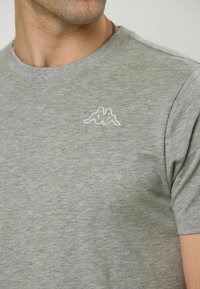 Grå t-skjorte med korte ermer laget av mykt stoff, med en liten hvit logo på brystet og klassisk rund hals.