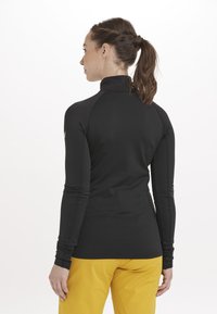 Sort langærmet performance top med høj hals, med tætsiddende design og tommelhuller. Tekstureret stof, synlige sømdetaljer.