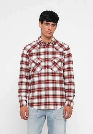 Camisa de franela de cuadros rojos y blancos con dos bolsillos en el pecho, cierre de botones y cuello puntiagudo, combinada con jeans de color azul claro.