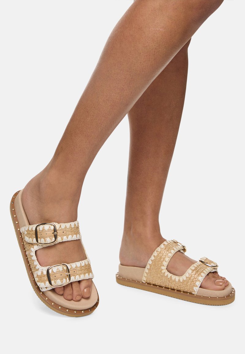 Tan and white slide sandals with two adjustable buckle straps, woven design texture, and a textured non-slip sole.