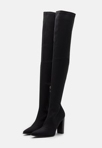 Botas negras de muslo alto hechas de un tejido elástico, con punta afilada y un tacón alto y grueso, con una cremallera lateral. Textura suave.